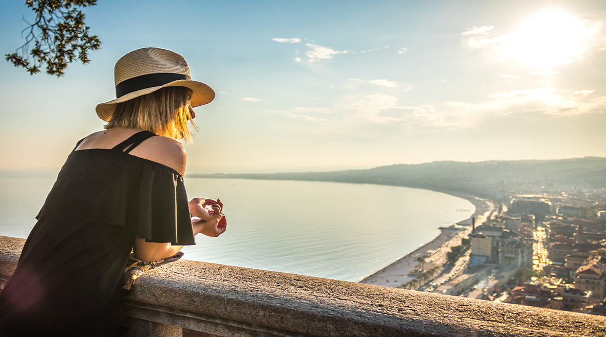 A woman in a straw hat gazes from a stone view point high above a bay and city